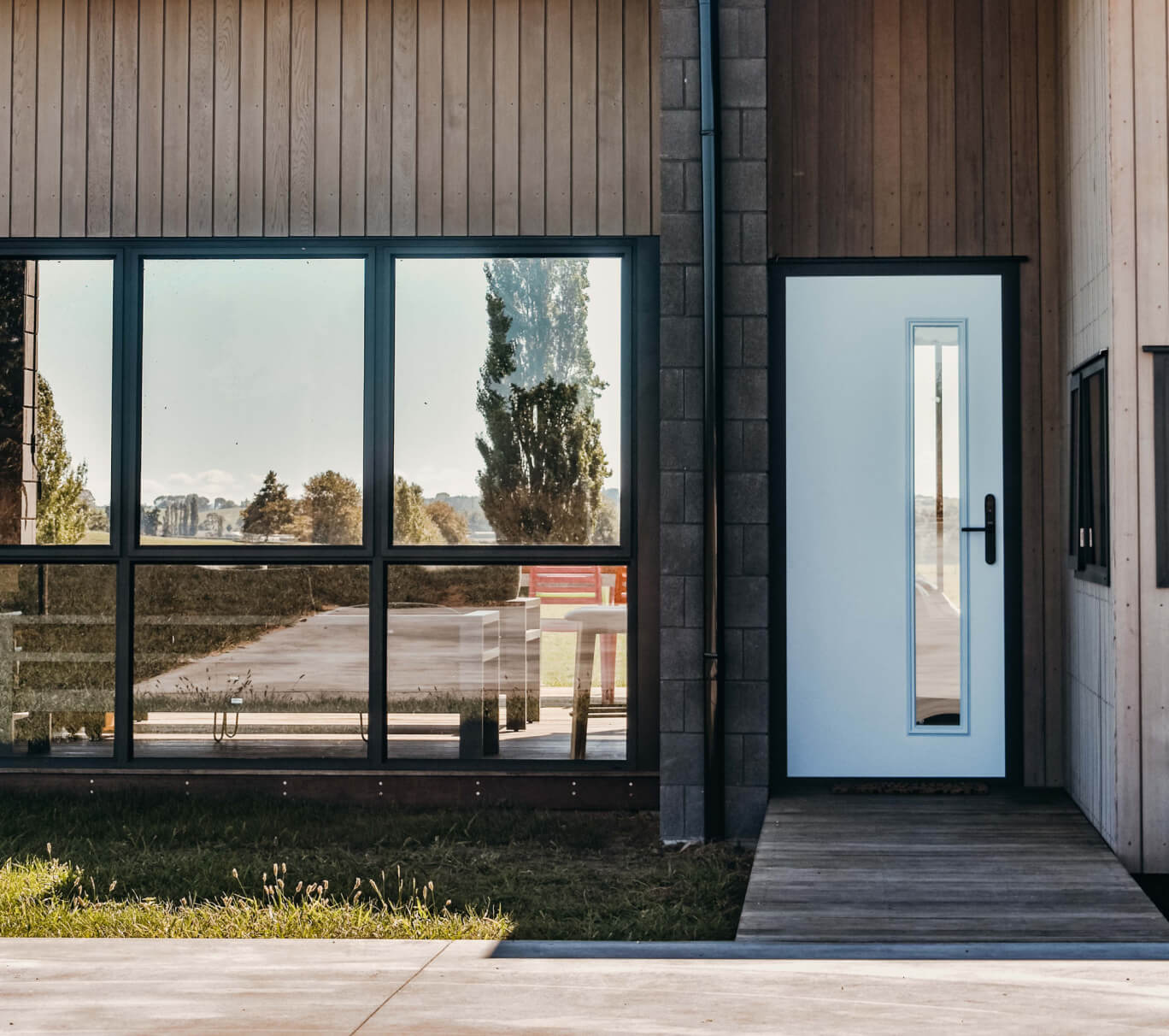 Duco single white hinged front door with a glass panel alongside black paneled windows set into the house